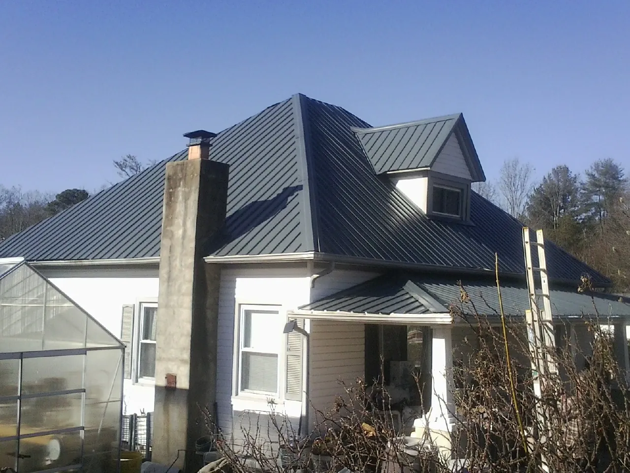 Dark blue standing seam metal roof on a white farmhouse with dormer — Slate & Tile Roof Repair by Roofing Brothers in Lusby