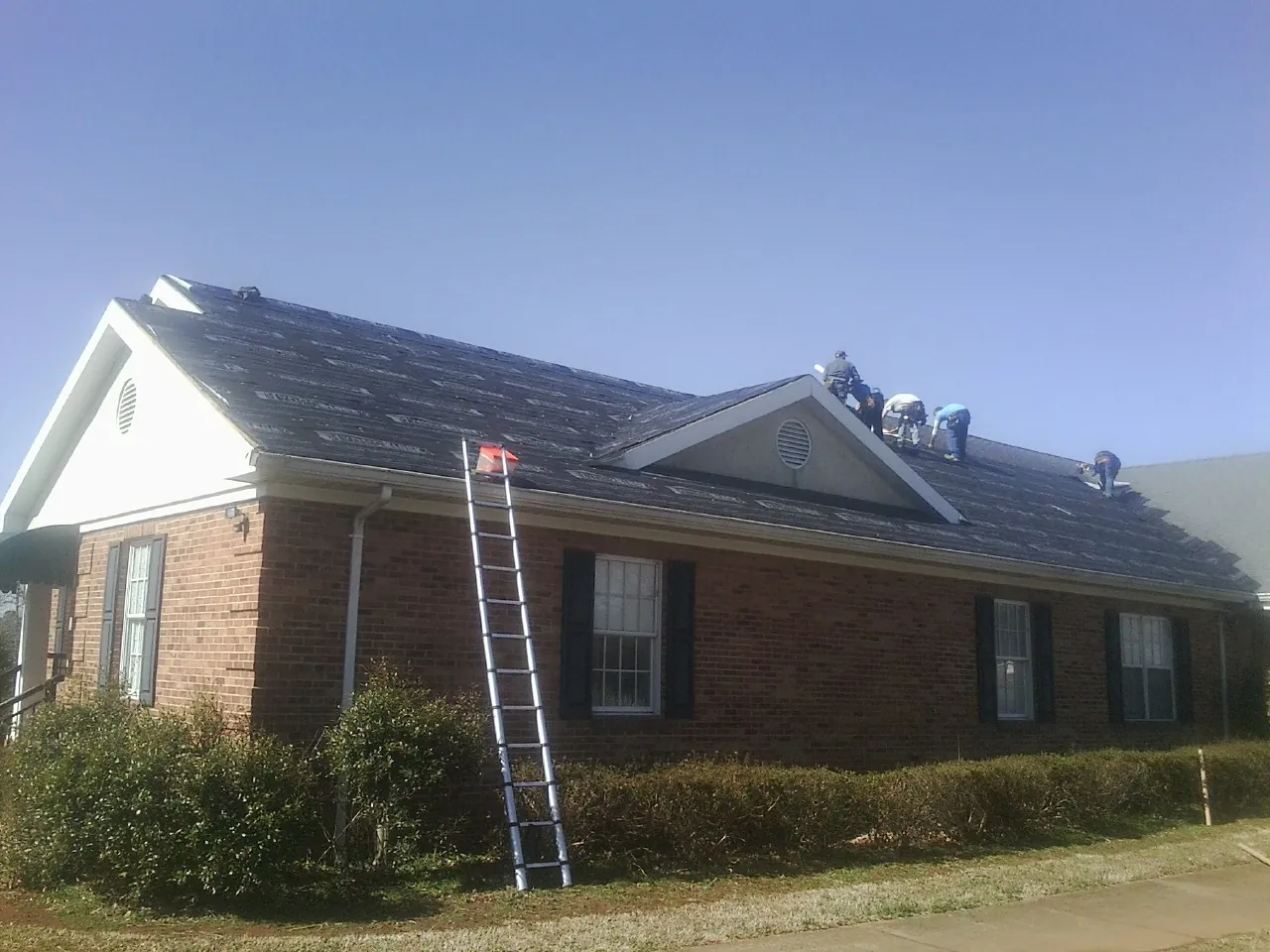 Crew tearing shingles off a brick ranch roof with a ladder set — Emergency Roof Repair work by our crew in Lusby
