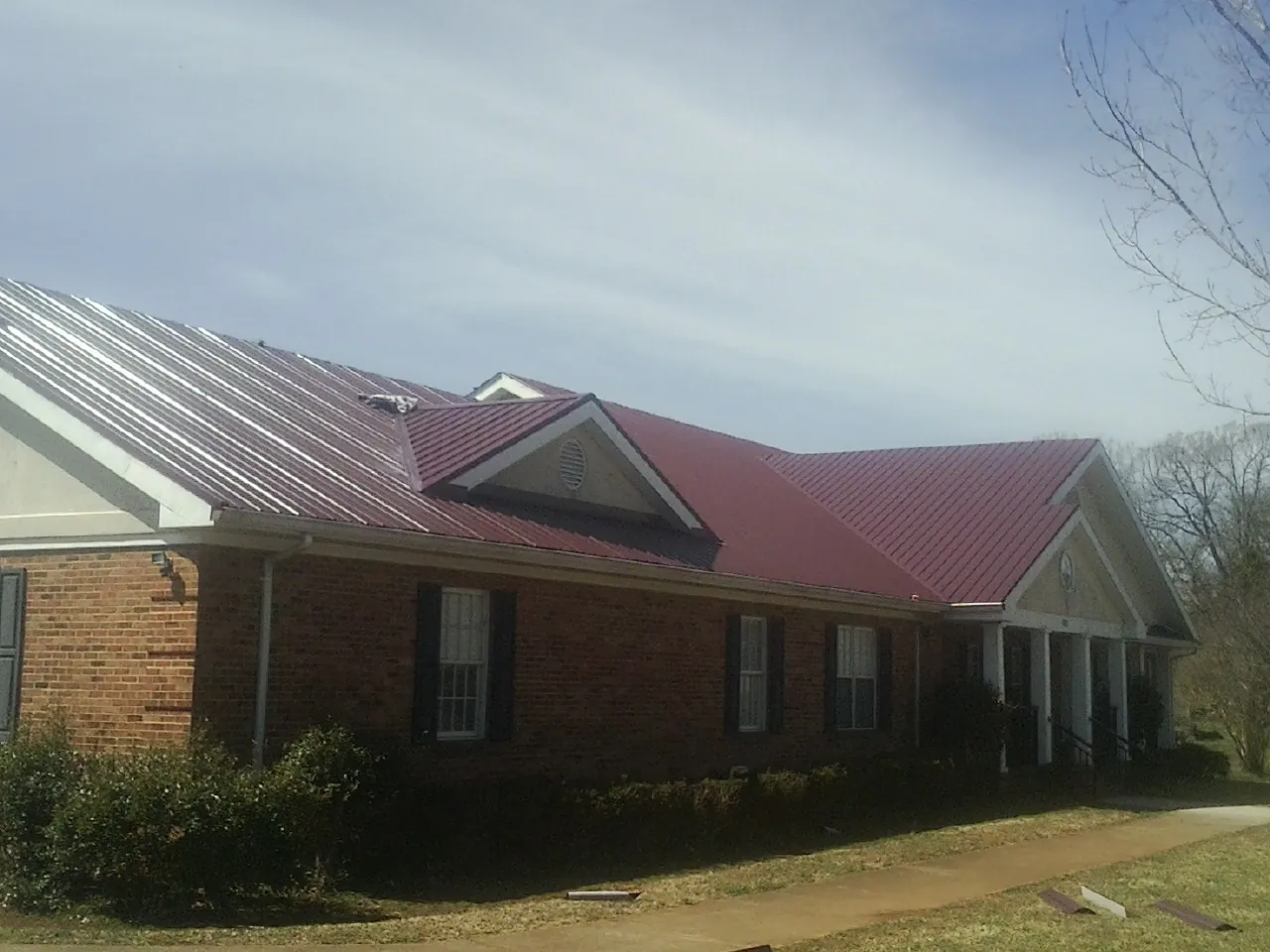 Red metal roof with gabled entries on a long brick building, from a Hail Damage Roof Repair job in Lusby