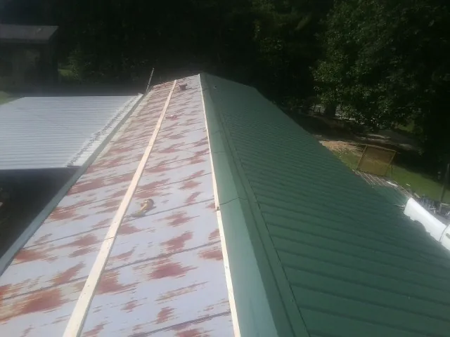 Old rusted panels beside newly installed green metal roofing — Wind Damage Roof Repair by Roofing Brothers in Lusby
