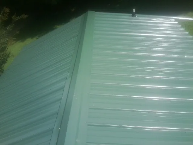 New green metal panels meeting at the ridge of a roof — Flat Roof Repair work by our crew in Lusby