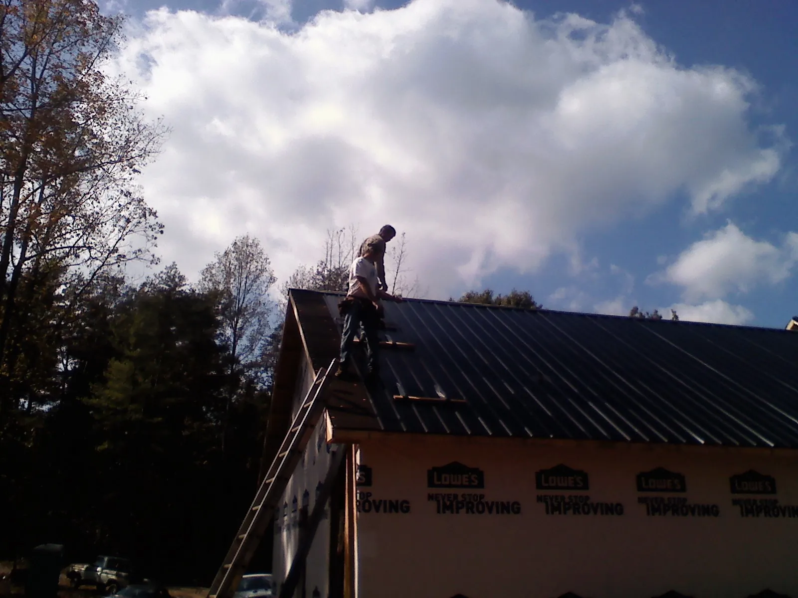 Roofer fastening dark metal panels high against a cloudy sky, from a Roof Inspection job in Lusby
