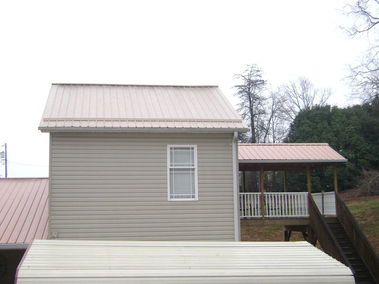 Tan metal roofs on a two story addition and attached porch, from a Roof Replacement job in Lusby